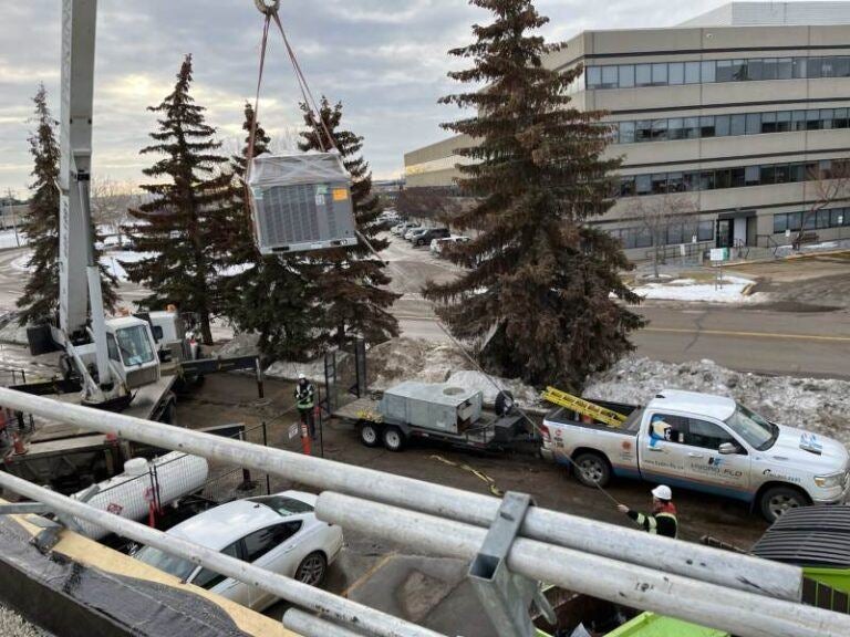 A crane lifts large equipment at a commercial HVAC installation site in Edmonton, AB