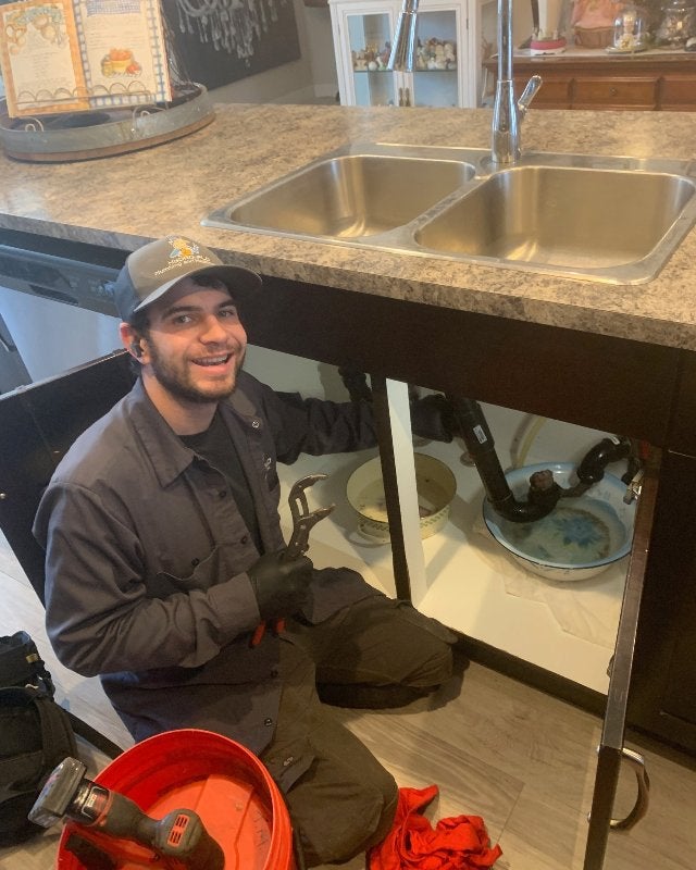 A Plumber from Hydro-Flo Plumbing & Heating Smiles While Working on a Kitchen Sink in Edmonton, AB